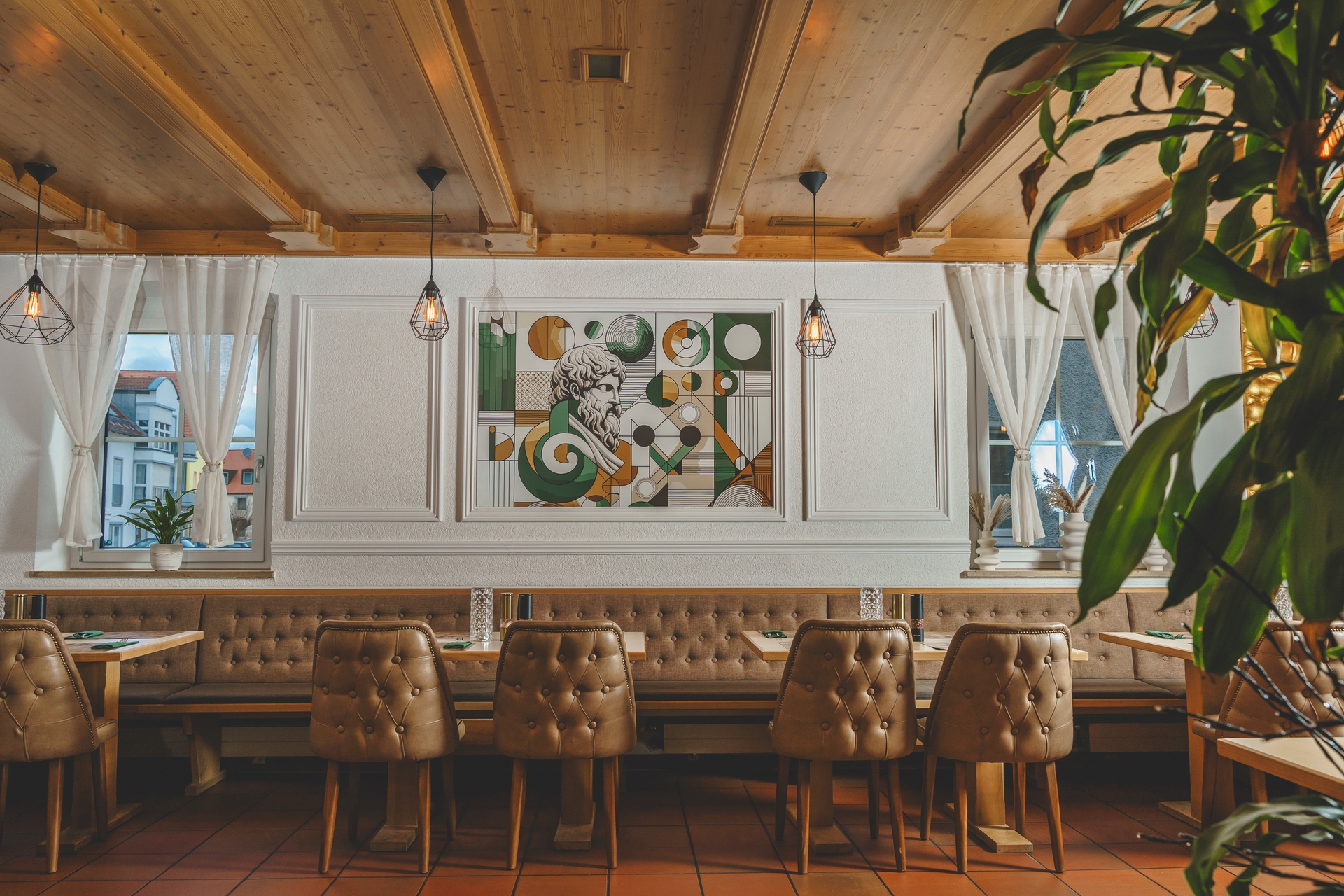 Stilvolles Interieur des Platon Restaurants in Berg mit bequemen gepolsterten Sitzbänken und Stühlen, elegantem Holzdekor und einer Wandkunst von Platon, der eine einladende und warme Atmosphäre für ein genussvolles Speiseerlebnis schafft.